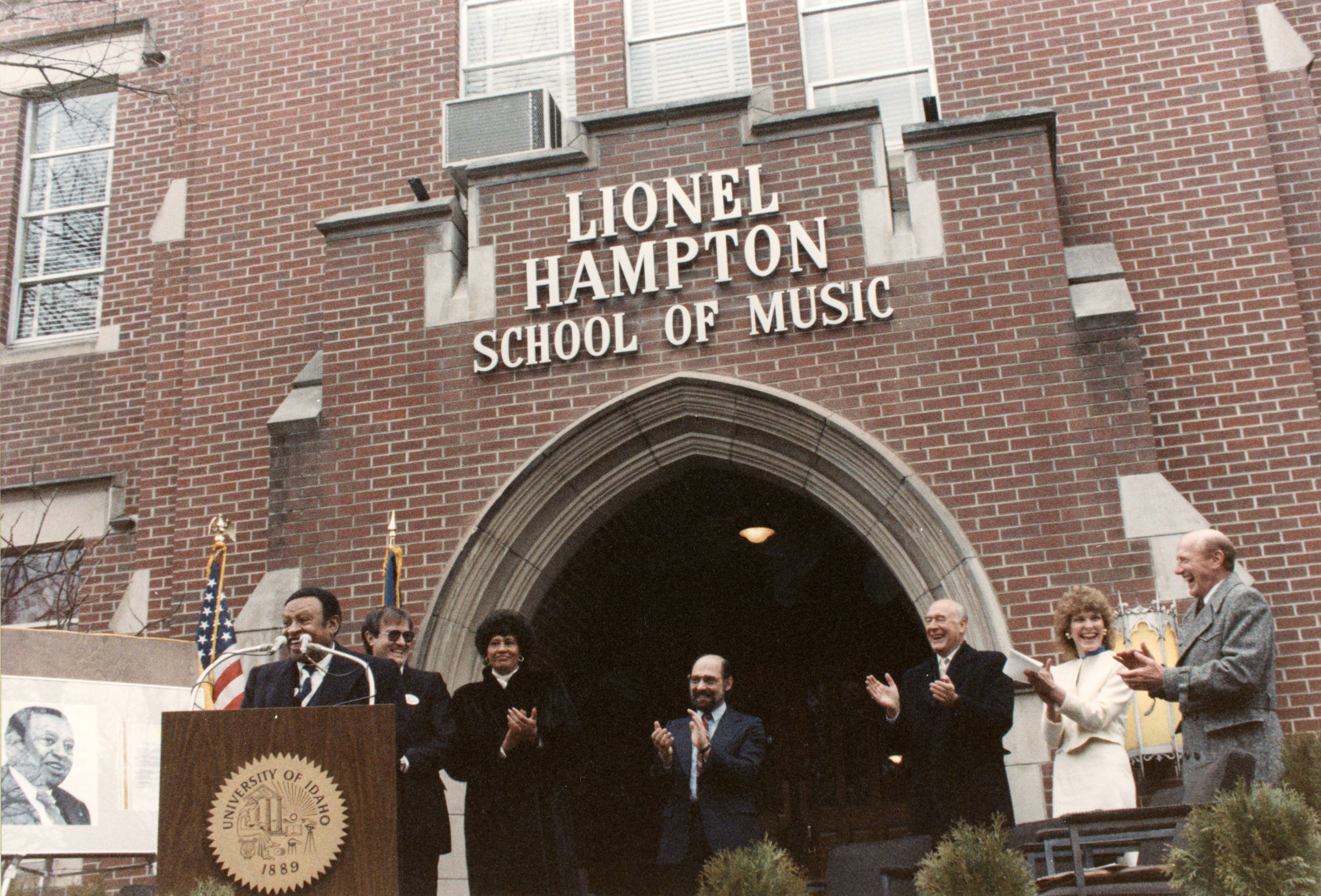 Lionel Hampton, a Black jazz singer, and others stand in front of the Lionel Hampton School of Music signage at the University of Idaho.