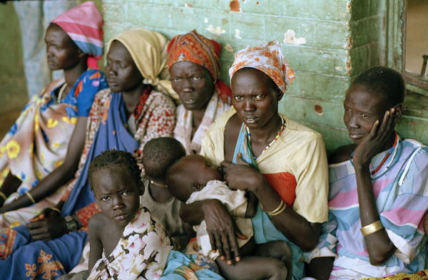 Many poor people gathered on the street, sitting against a wall