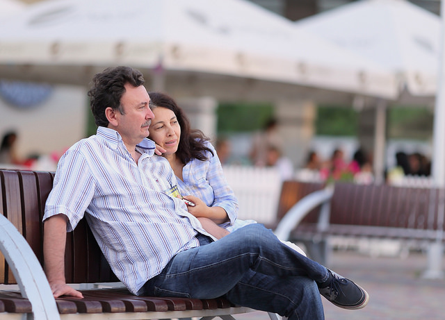 A woman leaning against her boyfriend on a public bench